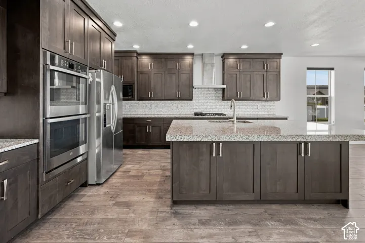 Kitchen featuring stainless steel appliances, dark wood-finish cabinetry, light-toned granite countertops, a white subway tile backsplash, and engineered wood flooring