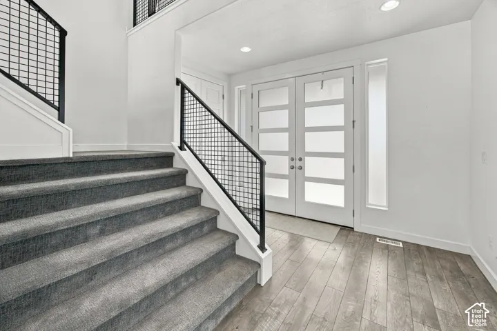 Wood-finish flooring, recessed lighting, double entry doors with frosted glass panels, and a staircase featuring grid-pattern metal railings