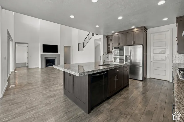 Engineered wood flooring throughout, kitchen island with stone countertop, stainless steel appliances, built-in cabinetry, and a fireplace with a stone surround
