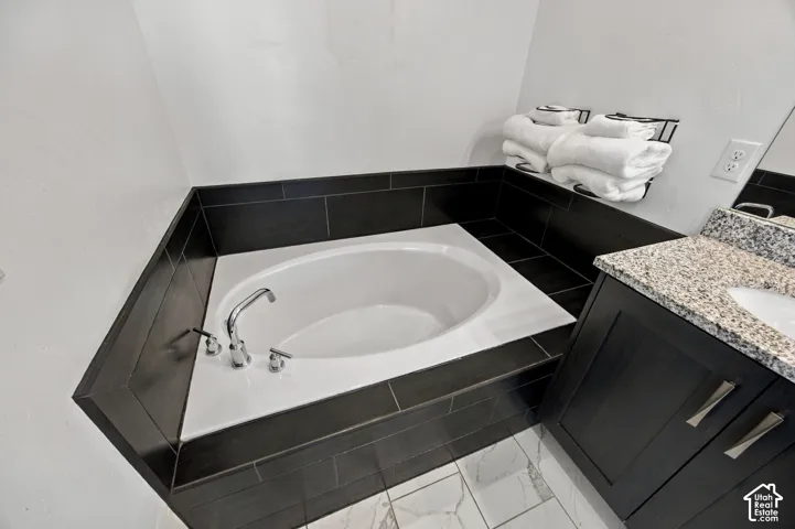 Primary Bedroom ensuite bathroom Soaking tub with dark tile surround, chrome fixtures, granite-look vanity, dark wood-finish cabinetry, and white tile flooring