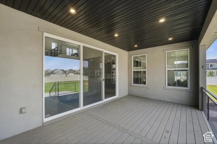 Covered patio featuring a slatted ceiling with recessed lighting, gray composite decking, stucco exterior, and sliding glass doors