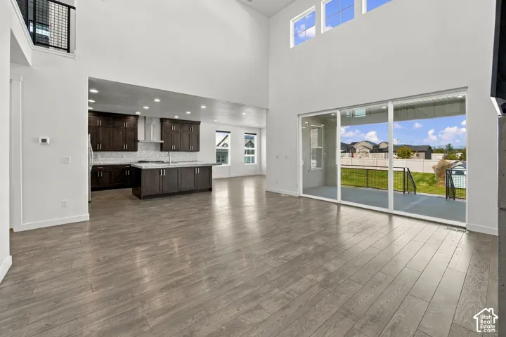 High ceilings, engineered wood flooring, a kitchen featuring dark wood cabinetry, a center island with a sink, and sliding glass doors leading to an outdoor patio