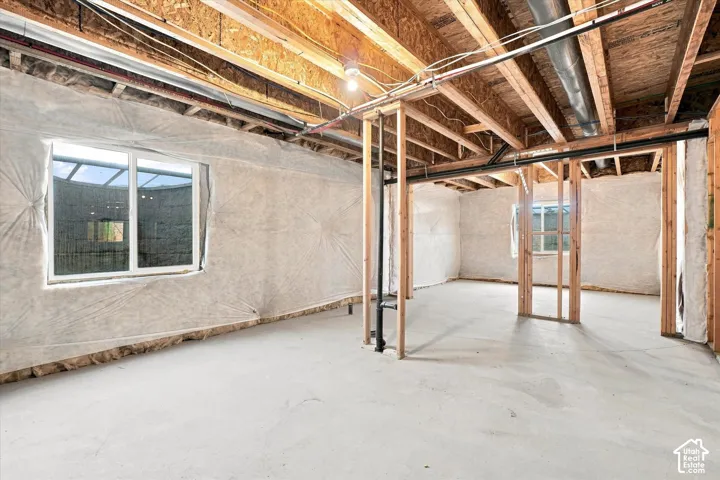 Unfinished lower level featuring exposed wood beam ceiling, concrete flooring, and multiple windows