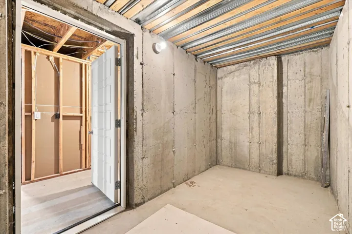 Possible Safe Room in Unfinished basement space featuring exposed concrete walls and ceiling joists