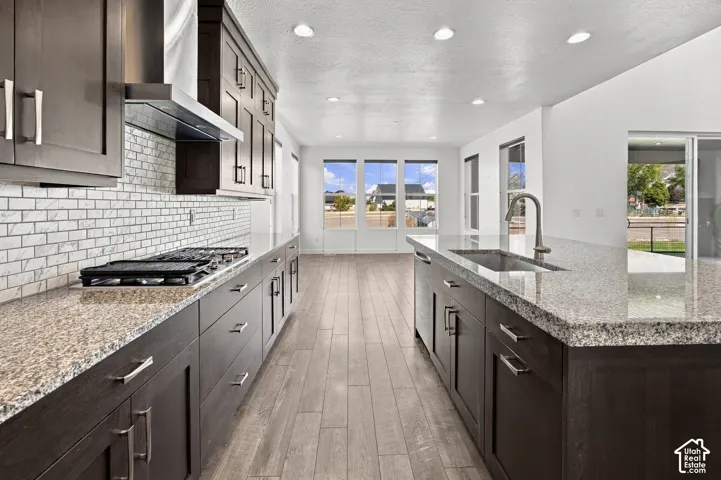 Kitchen featuring a gas range, stainless steel range hood, white subway tile backsplash, dark wood-finish cabinetry, and granite countertops