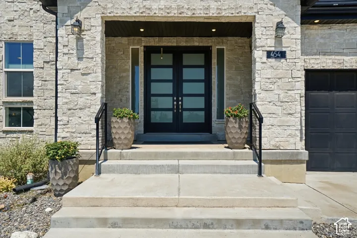 Stone veneer exterior featuring a modern double-door entry with frosted glass panels, concrete steps, and black metal railings