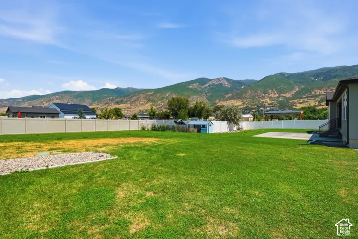 Expansive lawn area with a white privacy fence, mountain backdrop, and a concrete patio