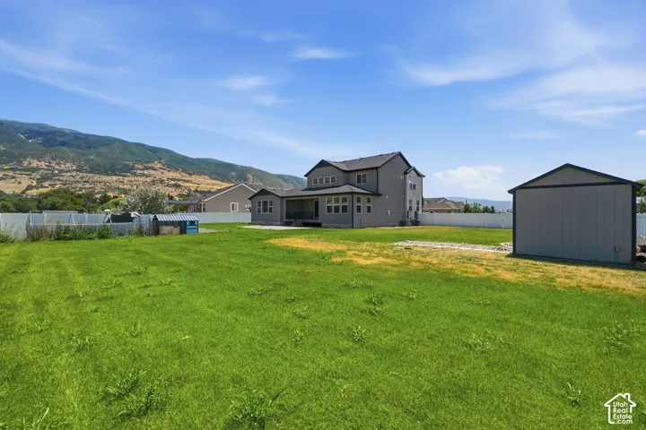 Expansive green lawn with a gray exterior two-story residence featuring multiple windows, a covered patio, and a separate storage shed