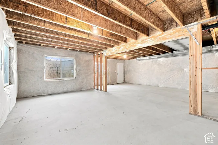 Unfinished basement featuring exposed wood joists, concrete flooring, and multiple windows