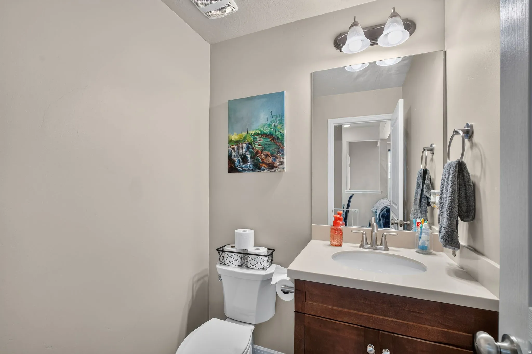 Bathroom featuring a single vanity with a white countertop, wood-finish cabinetry, and a chrome faucet