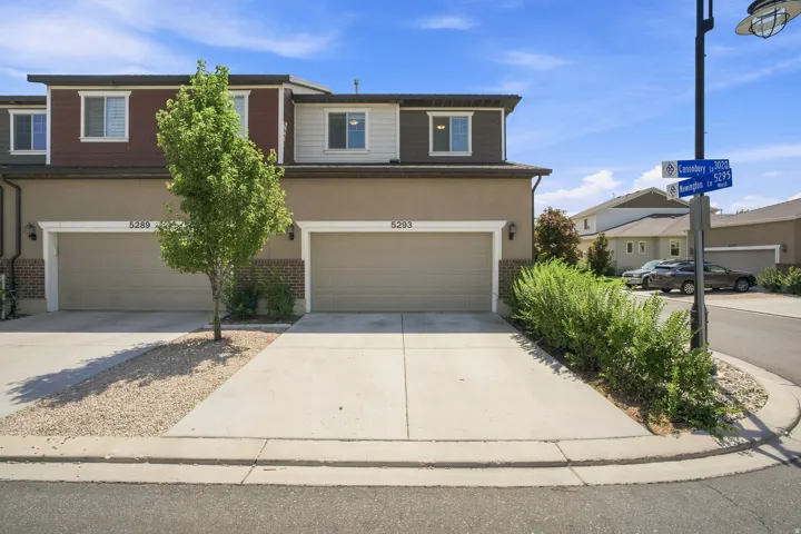 Contemporary townhome exterior featuring an attached two-car garage, concrete driveway, and a tan stucco finish
