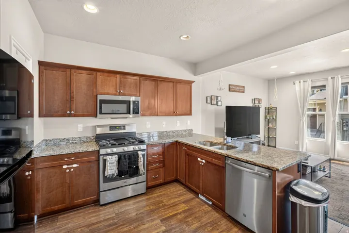 Kitchen featuring wood-finish flooring, wood cabinetry, stone countertops, and stainless steel appliances including a range, microwave, and dishwasher