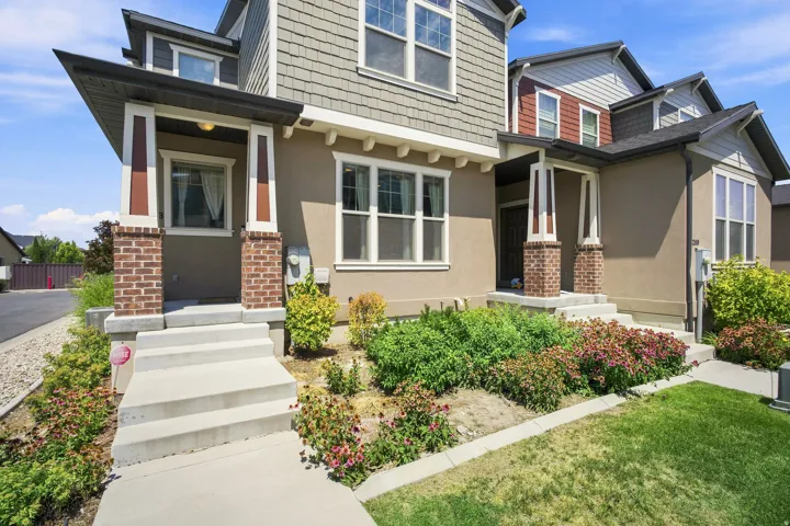 Multi-level facade featuring stucco and shingle siding, covered entryways with brick pillars, and mature landscaping