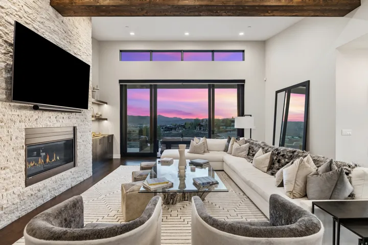 Spacious living area featuring a stacked stone fireplace, dark wood-finish flooring, and exposed ceiling beams