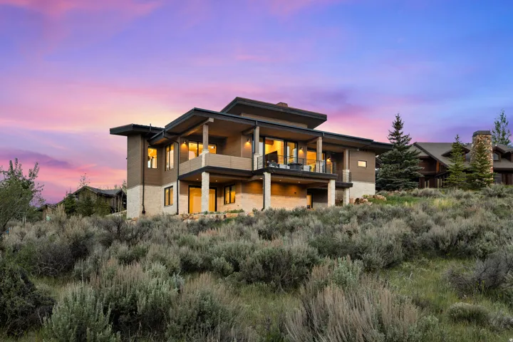 Contemporary multi-level residence featuring expansive windows, two elevated outdoor balconies, and a stone facade