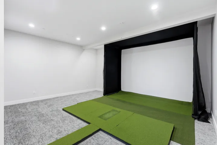 Dedicated indoor golf simulator space featuring a large white impact screen and artificial turf hitting area