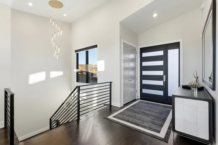 Modern entry featuring a dark wood-finish door with frosted glass panels, wood-finish flooring, and a contemporary chandelier