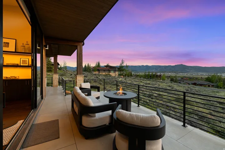 Expansive outdoor patio featuring a concrete surface, black metal railings, a gas fire pit, and a wide mountain backdrop