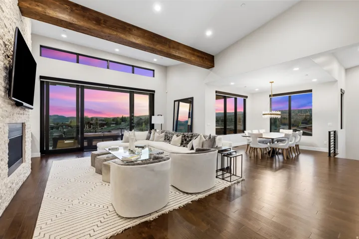 Spacious living area featuring high vaulted ceilings, exposed wood beams, a stone-clad fireplace, large sliding glass doors, and rich wood-finish flooring