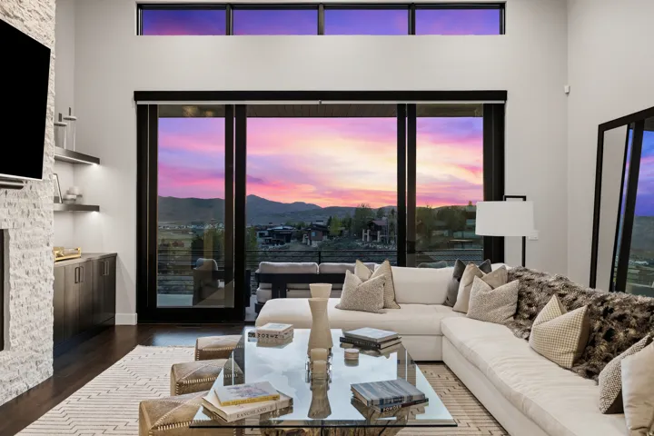 Expansive living room featuring large sliding glass doors, a transom window, a stone-clad fireplace surround, dark wood-finish flooring, and built-in shelving with integrated lighting