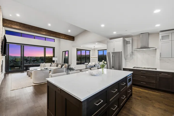 Open-concept kitchen and living area featuring wood-finish flooring, vaulted ceilings with exposed beams, and a stone accent wall