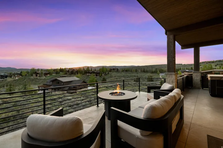 Spacious covered patio featuring a built-in fire pit, stone-clad columns, and a large hot tub