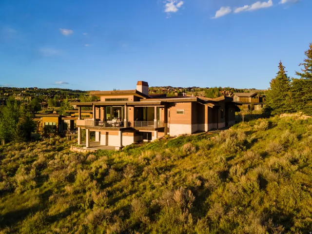 Contemporary residence featuring extensive glazing, multiple outdoor terraces, a stone and wood-panel exterior, and a prominent chimney structure