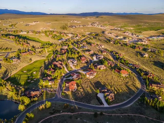Expansive mountain community featuring numerous residences, winding paved roads, golf course fairways, a water feature, and distant mountain ranges