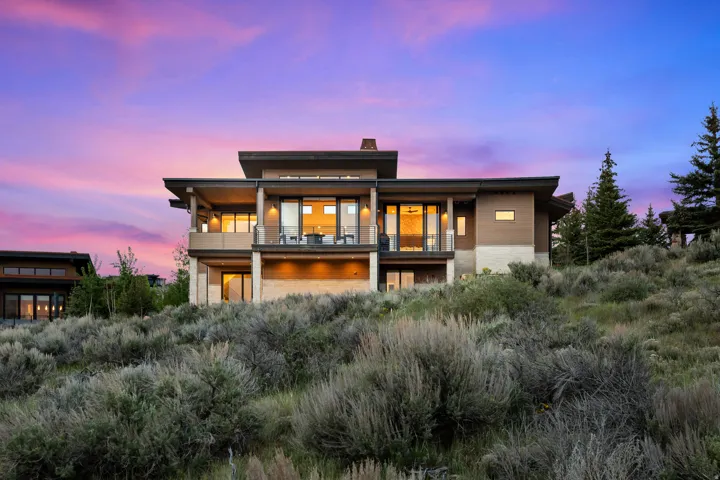 Multi-level contemporary residence featuring extensive glass doors, two upper-level balconies with glass railings, a covered patio, and a stone facade