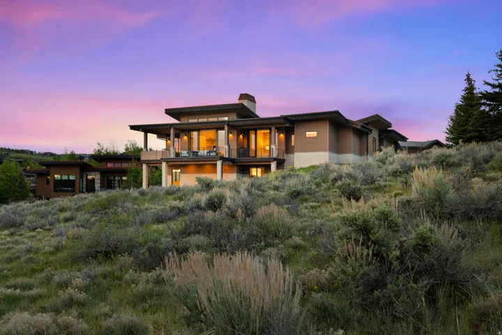 Contemporary multi-level residence featuring expansive windows, a large covered balcony, and a stone-clad base