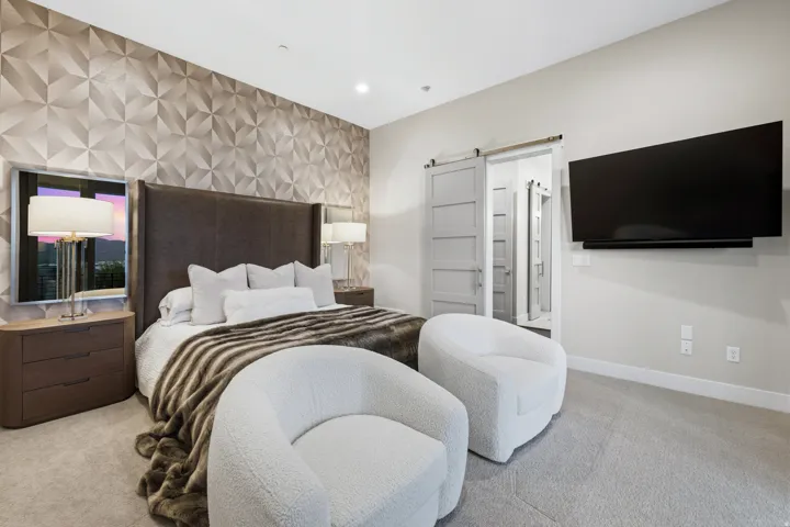 Bedroom featuring a textured accent wall with geometric patterns, light gray carpeting, and a modern barn door