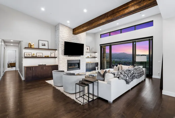 Spacious living area featuring a vaulted ceiling with exposed wood beam, a stone-clad fireplace, built-in shelving with lower cabinetry, and expansive glass doors opening to the exterior