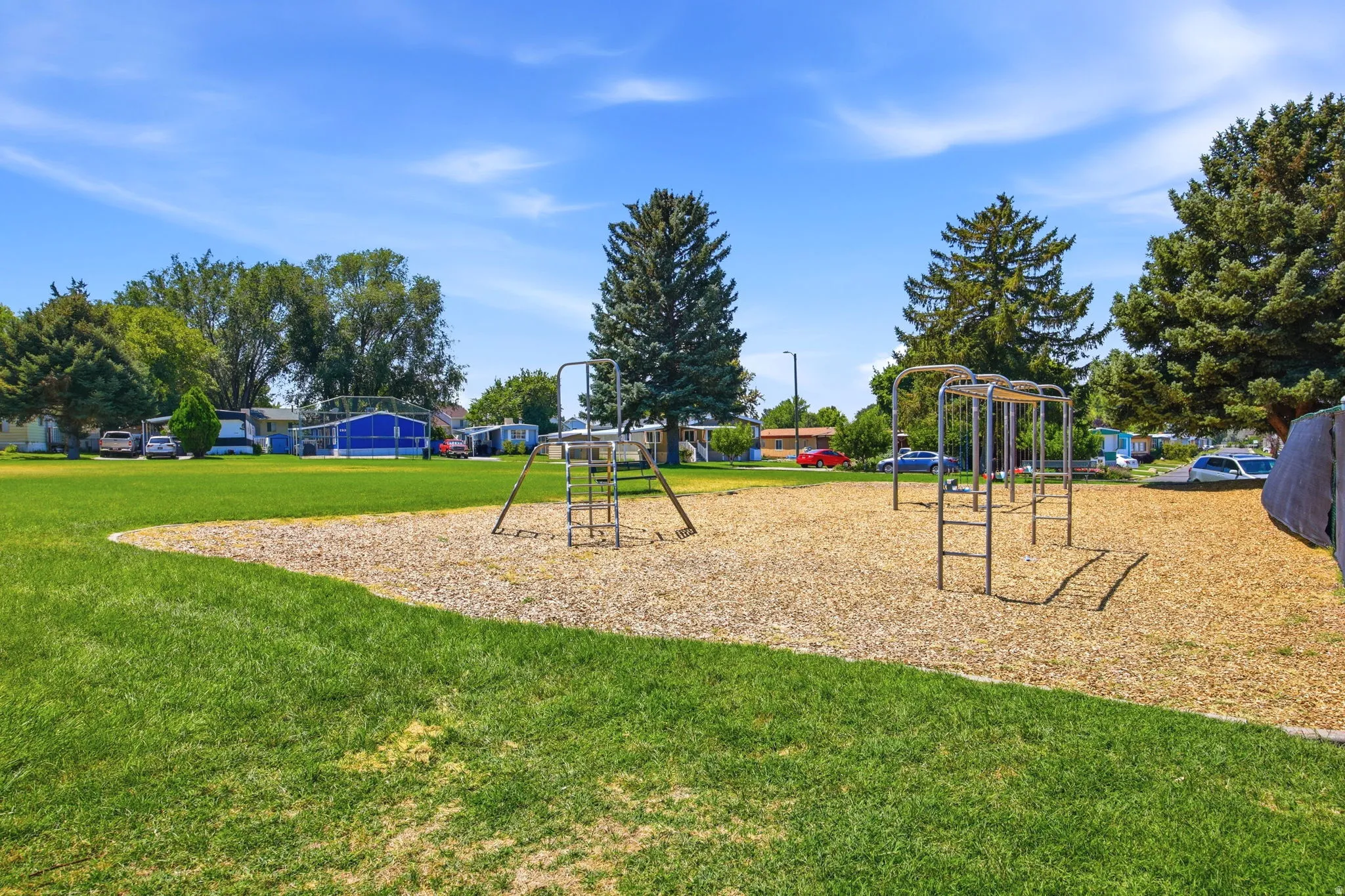 Expansive recreational grounds featuring multiple playground structures, a generous lawn area with mature tree coverage, and a dedicated mulch play surface