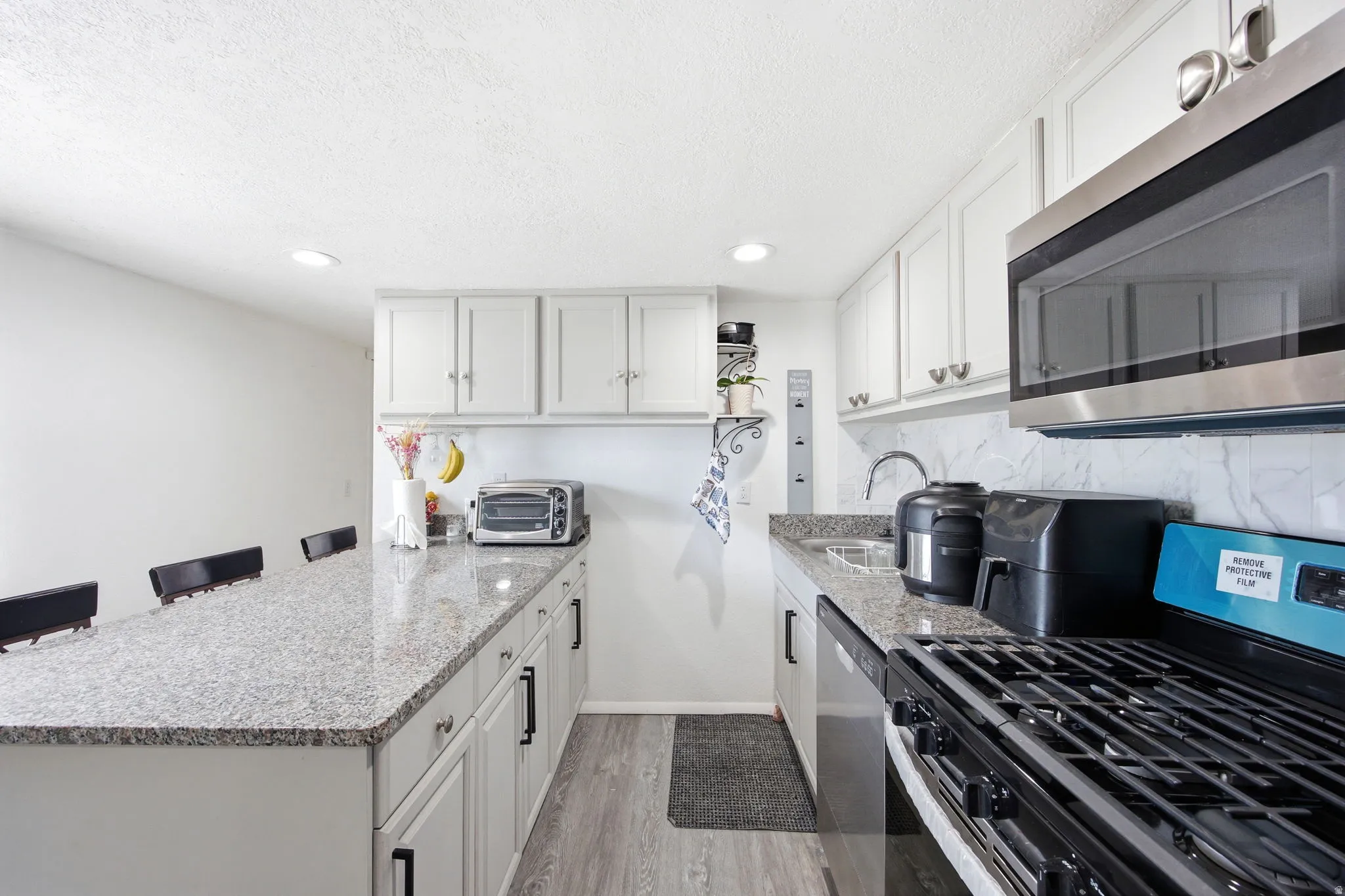 Kitchen featuring white cabinetry, speckled countertops, stainless steel appliances, wood-finish flooring, and recessed lighting
