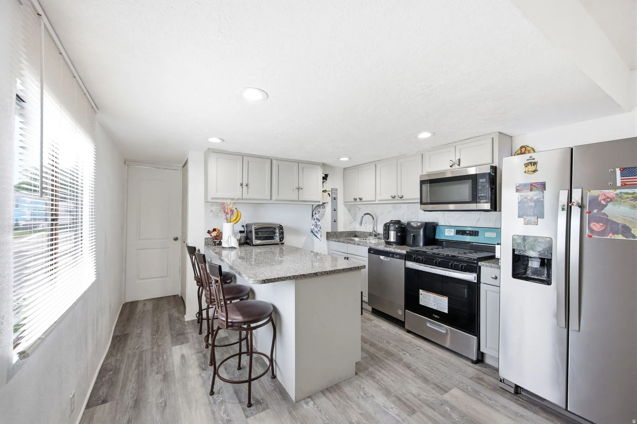 Contemporary kitchen featuring a granite-topped island with seating, stainless steel appliances, light gray cabinetry, and wood-finish flooring