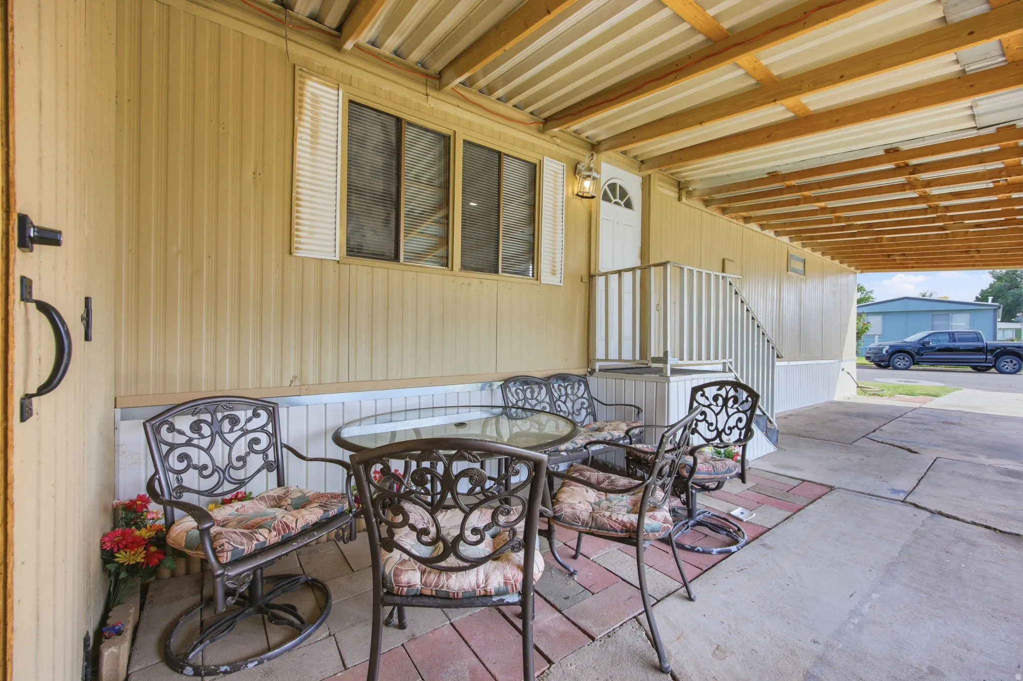 Covered patio featuring a corrugated metal ceiling with exposed wood beams, concrete flooring, and a brick paver accent