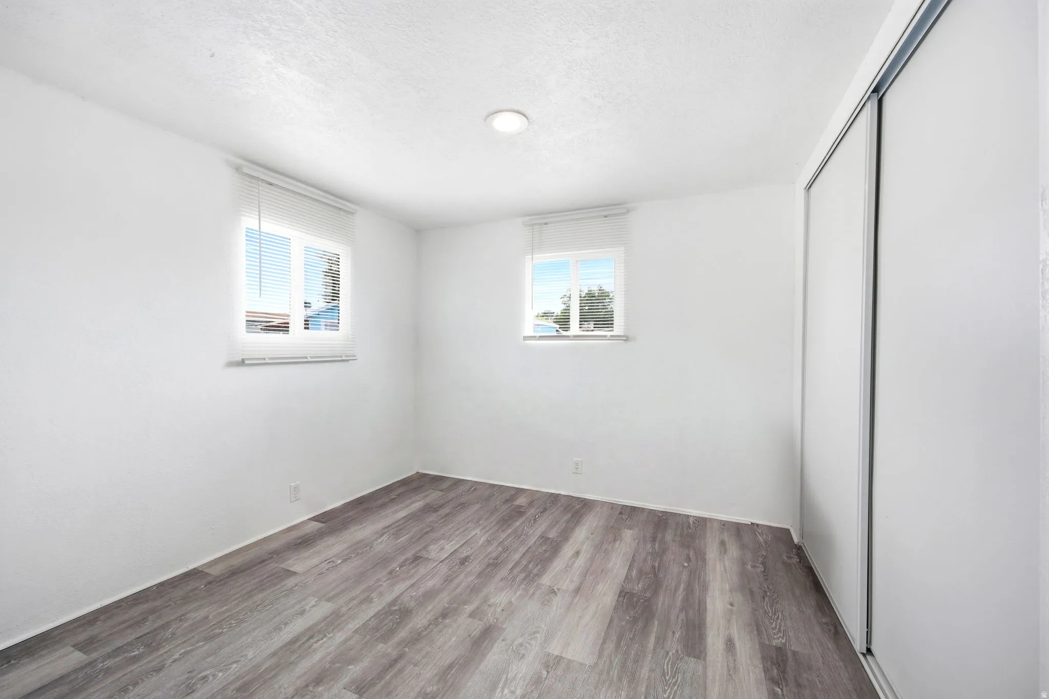 Interior space featuring wood-finish flooring, white walls, and two windows with blinds