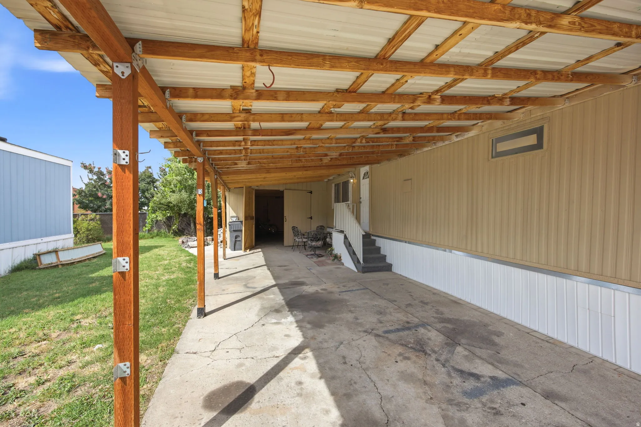 Carport structure featuring exposed wood beams and posts, corrugated metal roofing, and a concrete driveway
