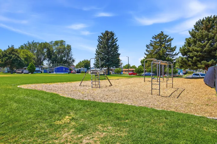 Expansive recreational grounds featuring multiple playground structures, a generous lawn area with mature tree coverage, and a dedicated mulch play surface