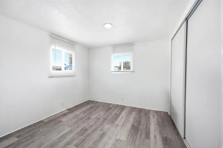 Interior space featuring wood-finish flooring, white walls, and two windows with blinds