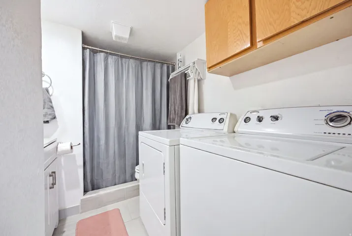 Dedicated laundry area featuring a white washer and dryer pair, light wood-finish upper cabinetry, and a shower with a gray curtain