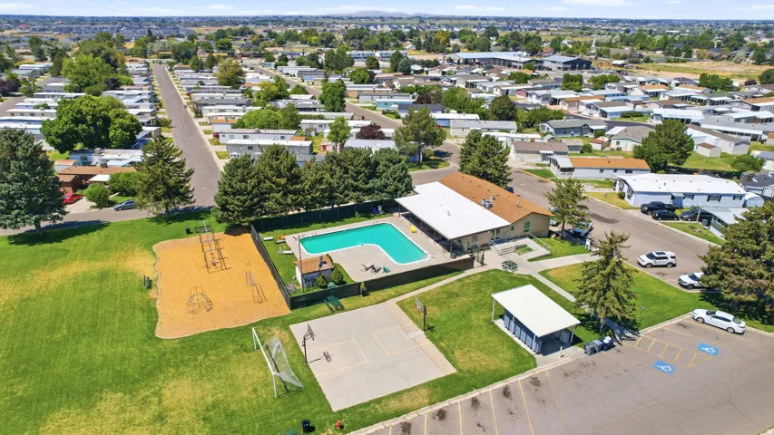 Aerial view of this recreational property featuring an in-ground swimming pool with surrounding concrete decking, a sand volleyball court, multiple storage structures, mature landscaping with established trees, and direct waterfront access