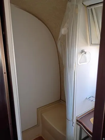 Compact bathroom featuring a shower stall with a built-in bench, a shower curtain, a wall-mounted mirror, a towel ring, and a corner sink with a dark-finish countertop