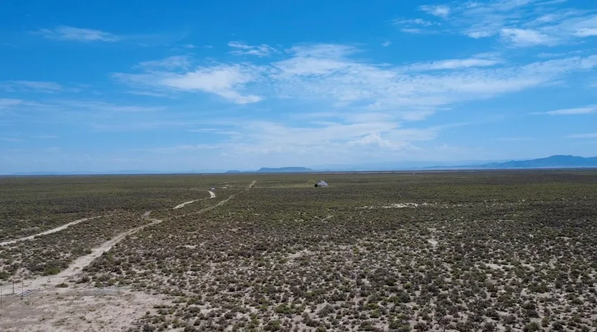 Expansive desert landscape with a distant structure and visible dirt track