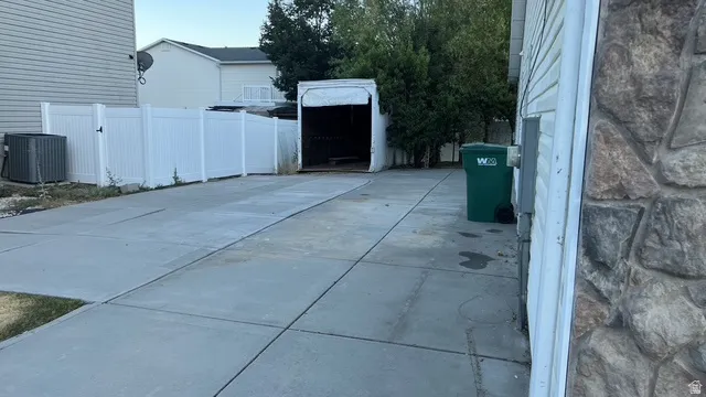 Extended concrete driveway with a white privacy fence and an open storage structure