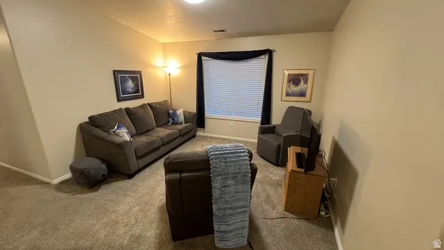 Carpeted interior space featuring a window with horizontal blinds, neutral-toned walls, and a recessed ceiling light fixture