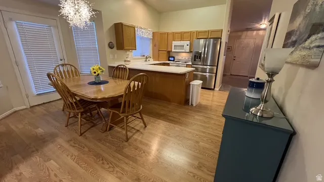 Open-concept kitchen and dining area featuring warm wood-finish flooring, a kitchen island with seating, light-toned countertops, and stainless steel appliances