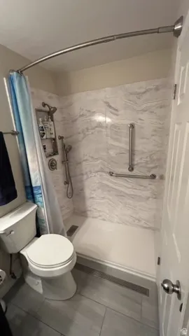 Walk-in shower featuring patterned wall panels, a linear drain, and grab bars