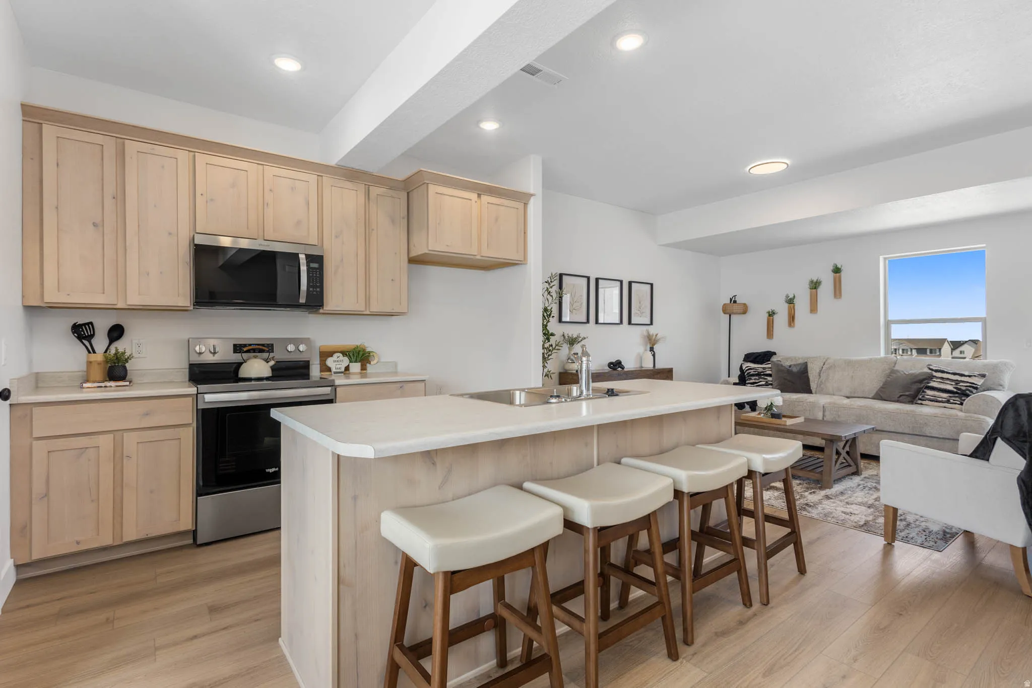 Open-concept kitchen featuring light wood cabinetry, stainless steel appliances, and a central island with countertop seating