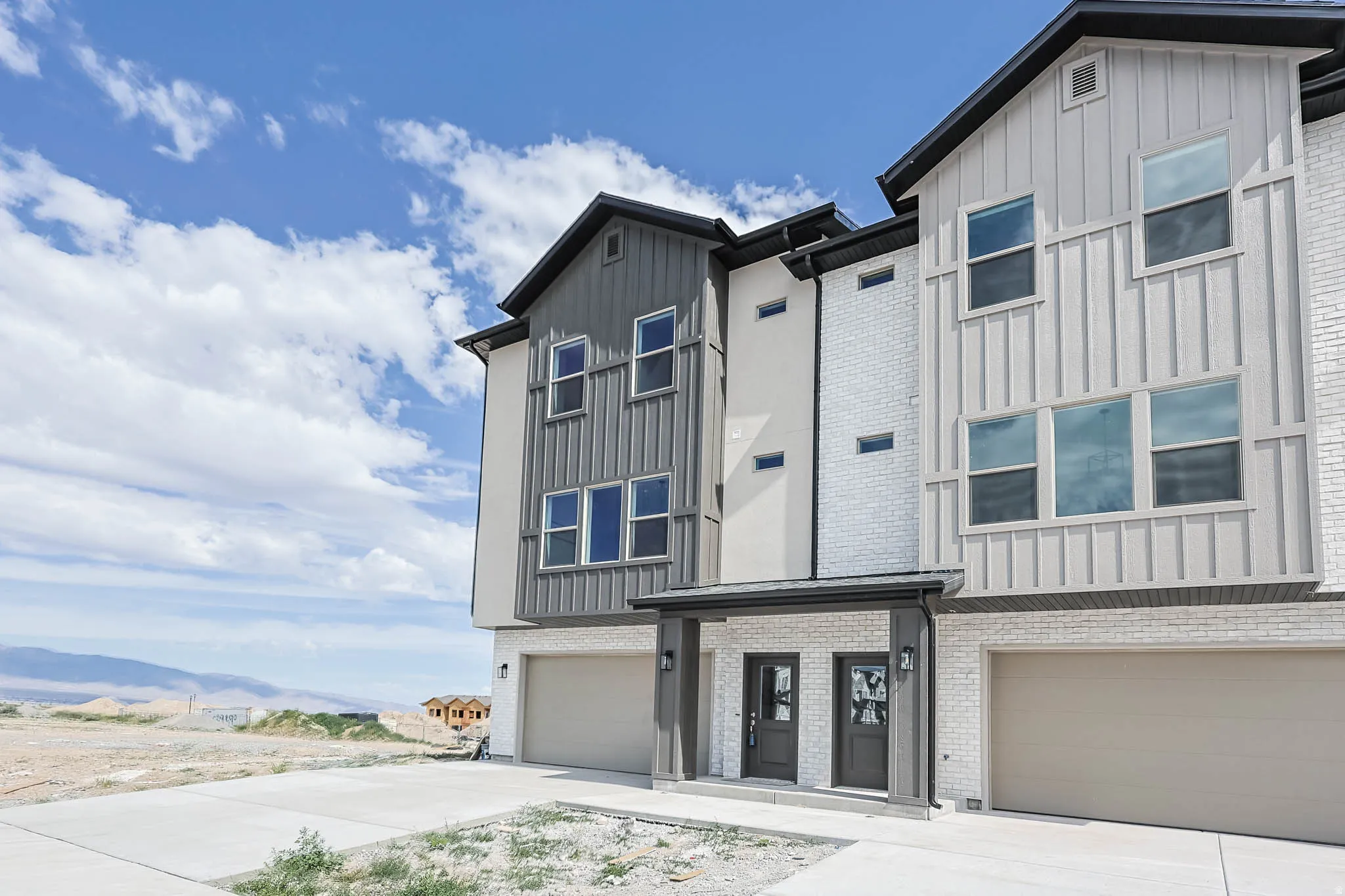 Modern multi-level exterior featuring vertical board and batten siding, white brick accents, and dark trim